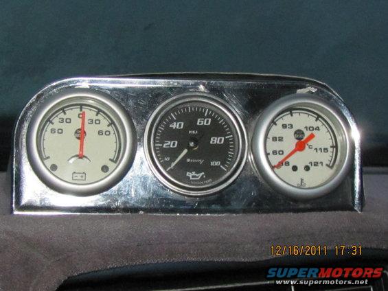 Chrome-bezeled triple gauge cluster with battery, oil pressure, and temperature gauges mounted on a dashboard