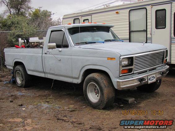 Gray Ford pickup truck parked in front of an RV. The truck has a chrome grille and a Ford badge