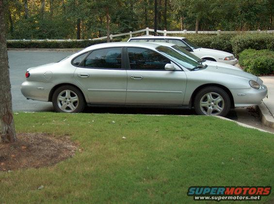 Silver sedan parked on grass, side view. Another white car is behind it