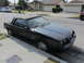 1985 Ford Mustang - A black 1985 Ford Mustang convertible is parked curbside on a sunny day in a suburban neighborhood.