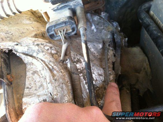 Close-up of damaged engine bay components with a finger pointing
