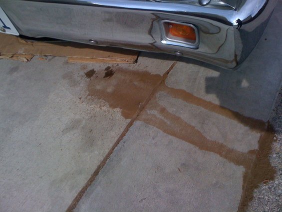 Chrome bumper with amber turn signal, sitting over cardboard with fluid stains on concrete
