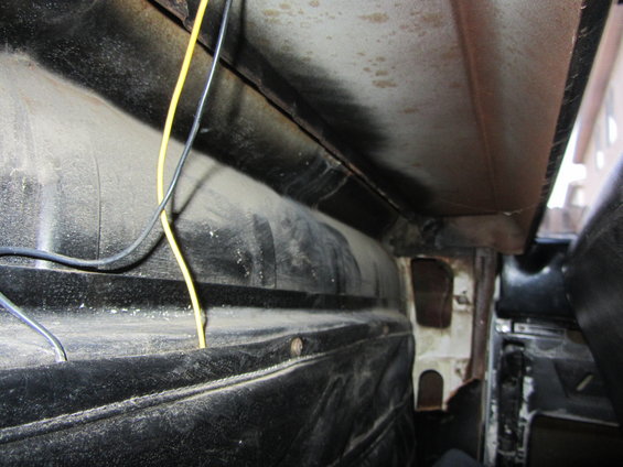 Close-up of dusty interior paneling and wiring in a vehicle. Shows black textured material and exposed metal