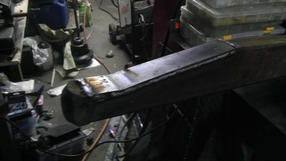 Welded metal beam with visible weld marks and a rounded end, angled view