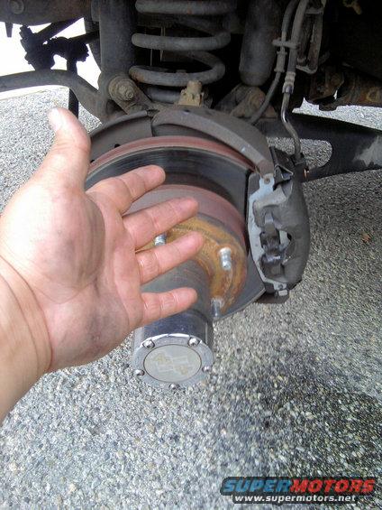 hand next to rear brake rotor and caliper assembly