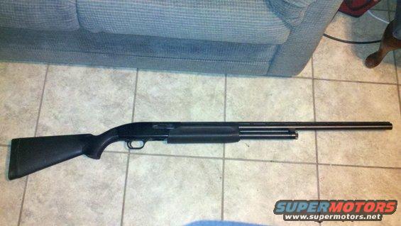 black pump-action shotgun lying on a tiled floor next to a couch