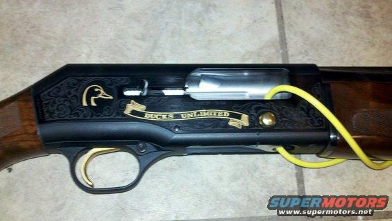 Shotgun receiver with Ducks Unlimited logo and engraved scrollwork. Gold trigger and yellow cord visible