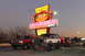 1994 Ford Bronco - Two lifted SUVs are parked in front of a retro diner with a large neon sign advertising hamburgers.