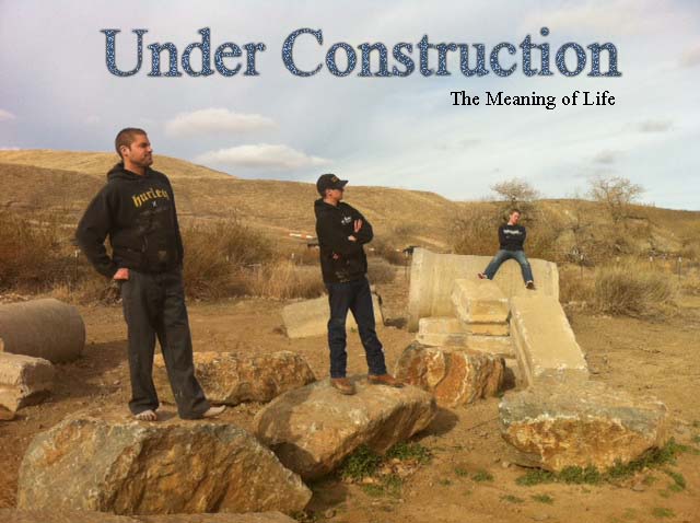 Three people stand in a rocky, outdoor area with concrete blocks. Text overlay reads 'Under Construction The Meaning of Life'