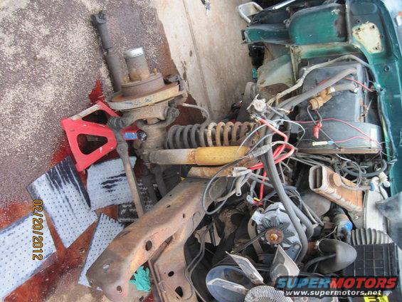 Disassembled green vehicle front suspension and engine components on concrete