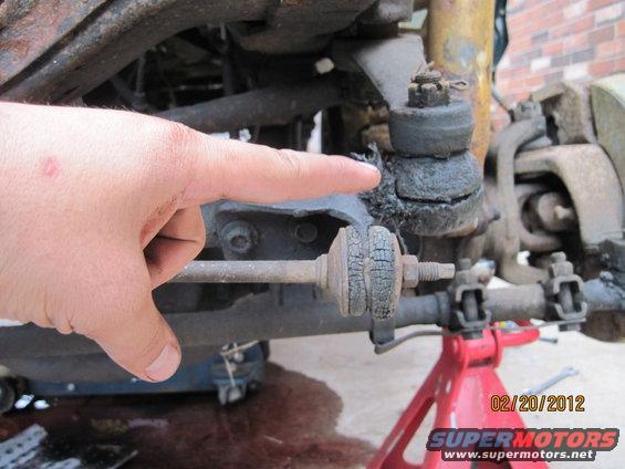 Hand pointing at a cracked suspension ball joint and sway bar link. Red jack stands visible