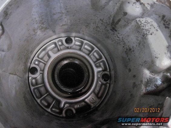 Close-up of a transmission housing with a circular flange and bolts. Splines are visible in the center opening. Date stamp reads 02/20/2012