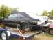 1987 Ford Mustang - A black 1987 Ford Mustang coupe is seen on a trailer, missing its wheels and undergoing some form of work or transport.