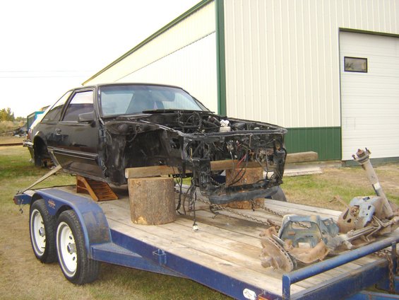 1987 Ford Mustang body on a trailer, engine removed, parts on trailer bed