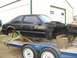 1987 Ford Mustang - A black 1987 Ford Mustang body is being transported on a trailer, stripped down and missing its front end.