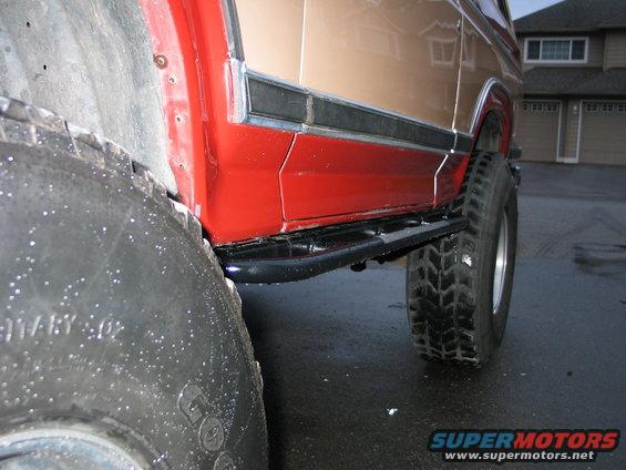 Side view of a red and tan Ford Bronco with large off-road tires and running boards