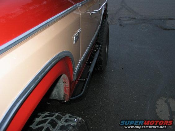 Side view of a tan and red 1984 Ford Bronco with large tires and running boards