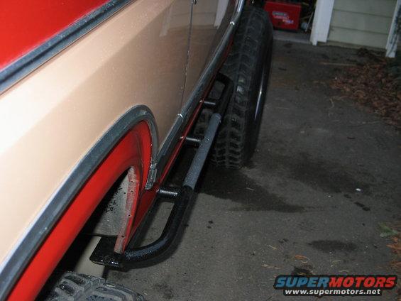 Side view of a 1984 Ford Bronco showing tan paint, red fender flares, and black rock sliders