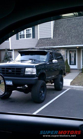 Lifted dark green Ford Bronco parked in front of a house. License plate visible