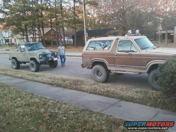 guy standing next to lifted tan pickup truck, brown SUV parked on side of road