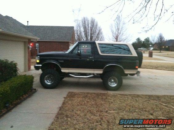 Black and tan Ford Bronco with lifted suspension and aftermarket wheels parked in a driveway