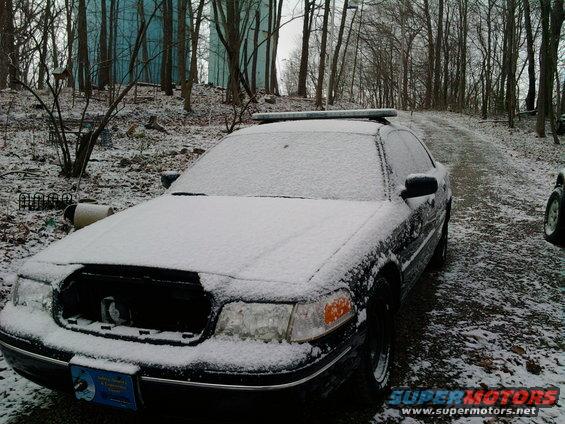 2001 Ford Crown Victoria covered in snow, front view, partially obscured by snow