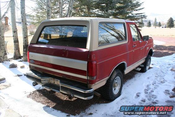 Red Ford Bronco with tan top parked in snow, rear view