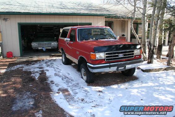 Red 1990 Ford Bronco 4x4 parked in front of a garage with snow on the ground