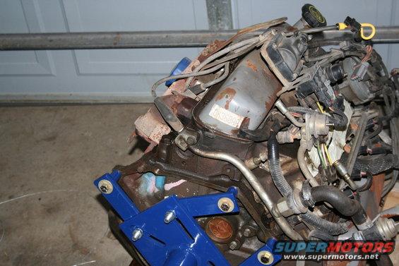 Engine block assembly with various hoses, wires, and a blue engine stand