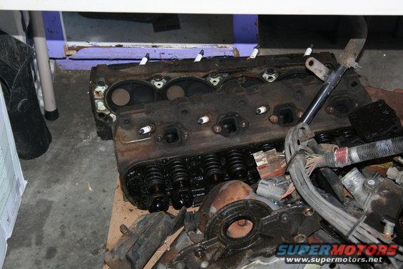 Engine block with spark plugs, wiring harness, and valve springs. Dirty and appears used