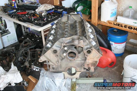 Engine block on stand with tools and supplies in background. Supermotors.net logo visible