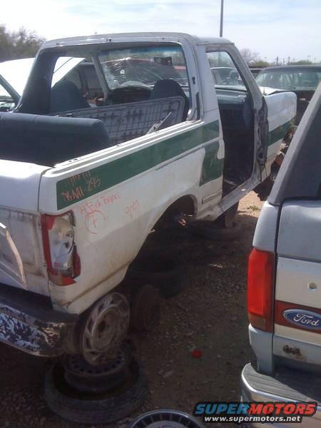 White 1979 Ford Bronco with green stripe, missing doors and wheels, parked in a junkyard