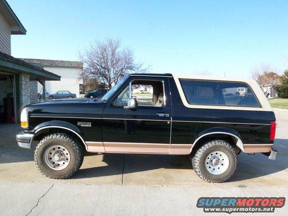 Black Ford Bronco with tan top and trim, parked outside a garage