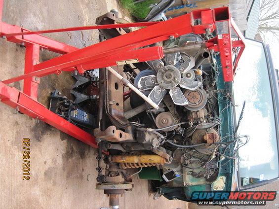 Engine being lifted out of a green vehicle by a red engine hoist. Date stamp 02/26/2012
