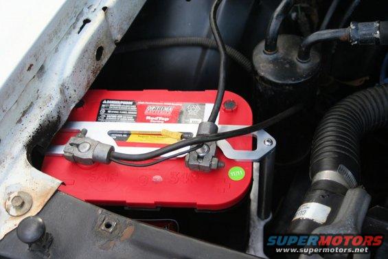 Red Optima battery with metal bracket and cables in engine bay