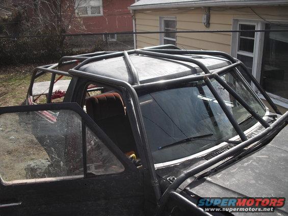 Black Ford Bronco with a custom roll cage, driver's door open, muddy tires visible through the window