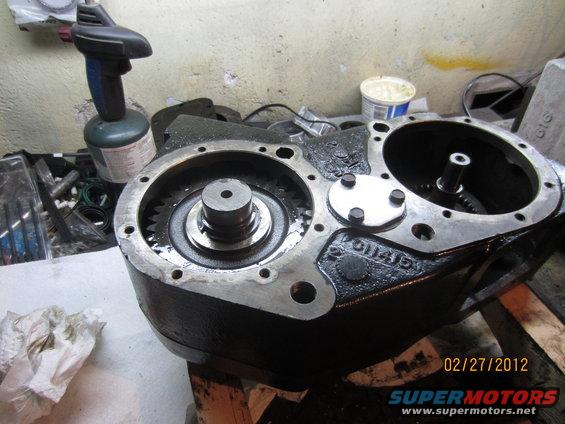 Black transfer case with visible gears and mounting bolts, on a workbench