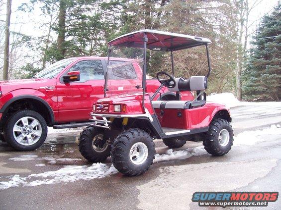 Red golf cart with off-road tires parked next to a red pickup truck
