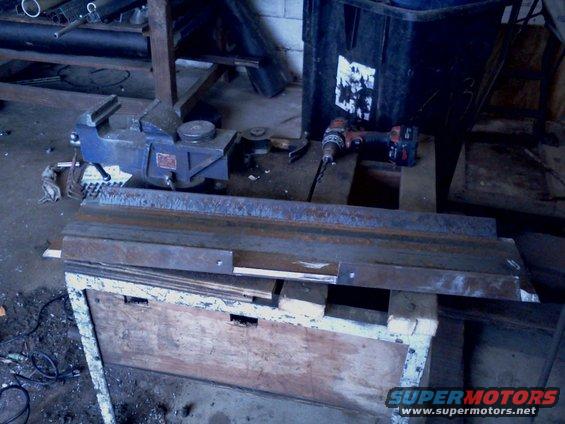 Workbench with a blue vise, drill, and metal parts in a workshop