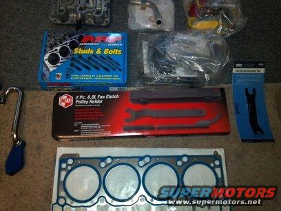 Assortment of automotive parts including ARP studs & bolts, a fan clutch pulley holder, and a head gasket