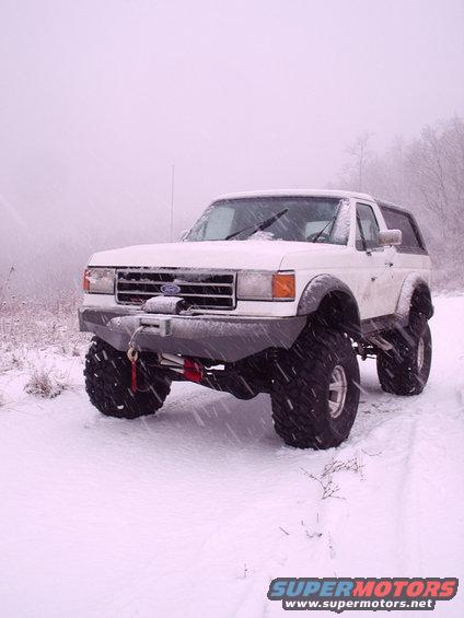 1991 Ford Bronco with large tires and custom front bumper with winch, parked in the snow