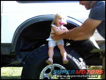 Child sitting on a large tire with a man's arm visible