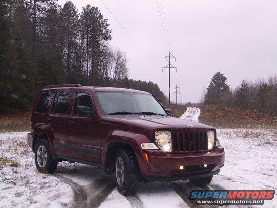 Maroon Jeep Liberty parked on a snowy dirt road with trees and power lines in the background