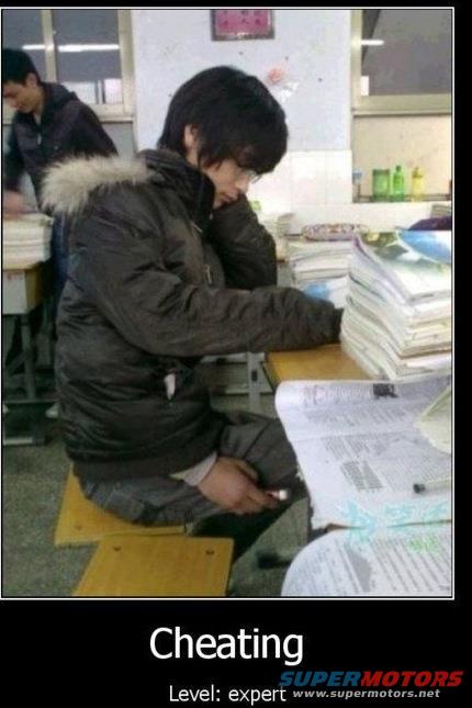 Student in a classroom, head down on a desk, holding a phone, surrounded by books