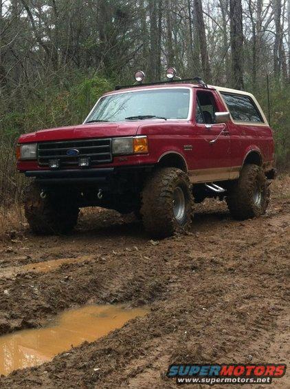 Red Ford Bronco with off-road tires stuck in mud, front 3/4 view