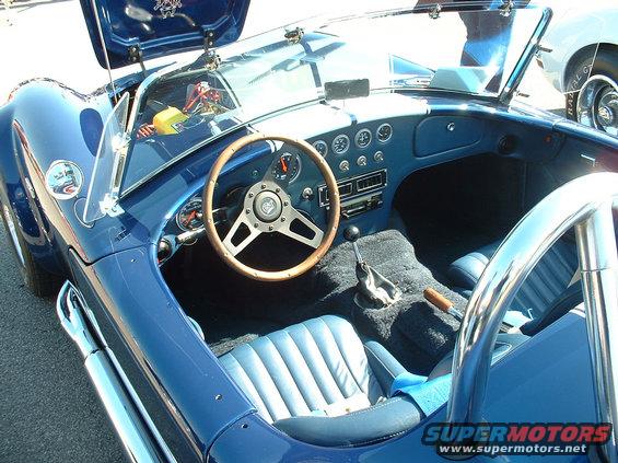 Blue convertible sports car interior with wood-rimmed steering wheel, dashboard gauges, and bucket seats