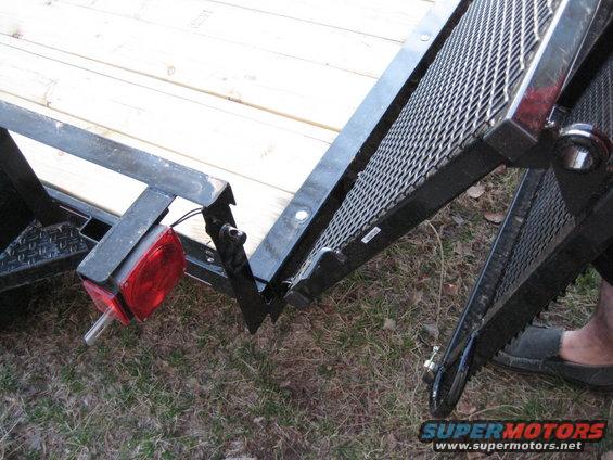 Close-up of a trailer ramp hinge with wooden deck visible