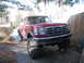 1996 Ford F-250 - A red pickup truck with large tires is parked in a driveway next to a wooden fence.