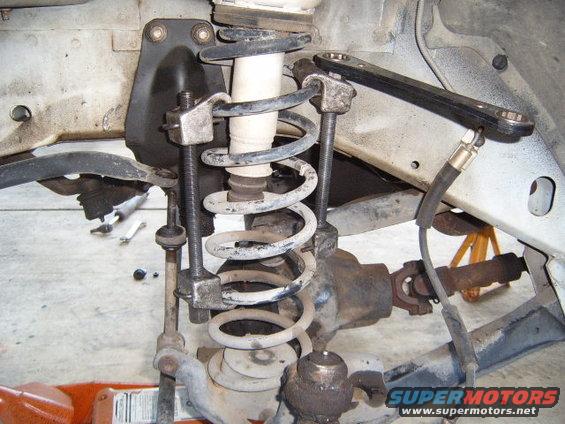 Spring compressor tool attached to vehicle's front suspension coil spring and shock absorber