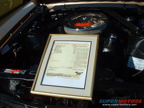 Framed window sticker for a Ford Mustang sits on top of an engine bay